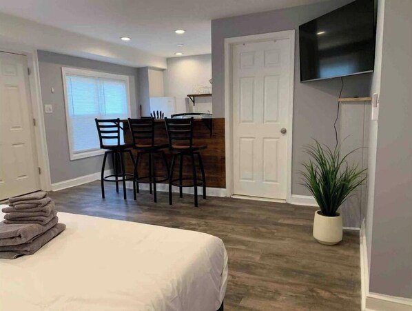 A bedroom with a bed, a desk with chairs, a television, and a potted plant.