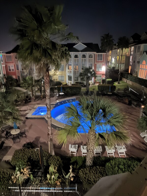 A pool area with lounge chairs, a palm tree, and a building with balconies.