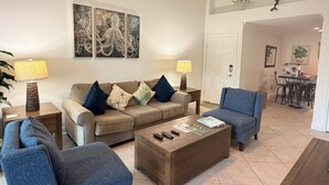 Una sala de estar con un sofá color crema, dos sillones azules, una mesa de centro y un ventilador de techo.