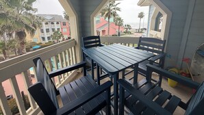 Un balcón con mesa y sillas de madera, con vistas a una zona residencial con casas coloridas y palmeras.