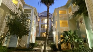 Un patio central con una palmera, rodeado de edificios con balcones y un cielo despejado.
