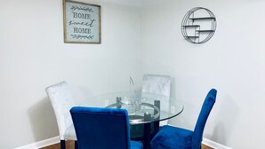 En matplats med ett glasbord omgivet av blå stolar, en vit stol och en inramad skylt på väggen.