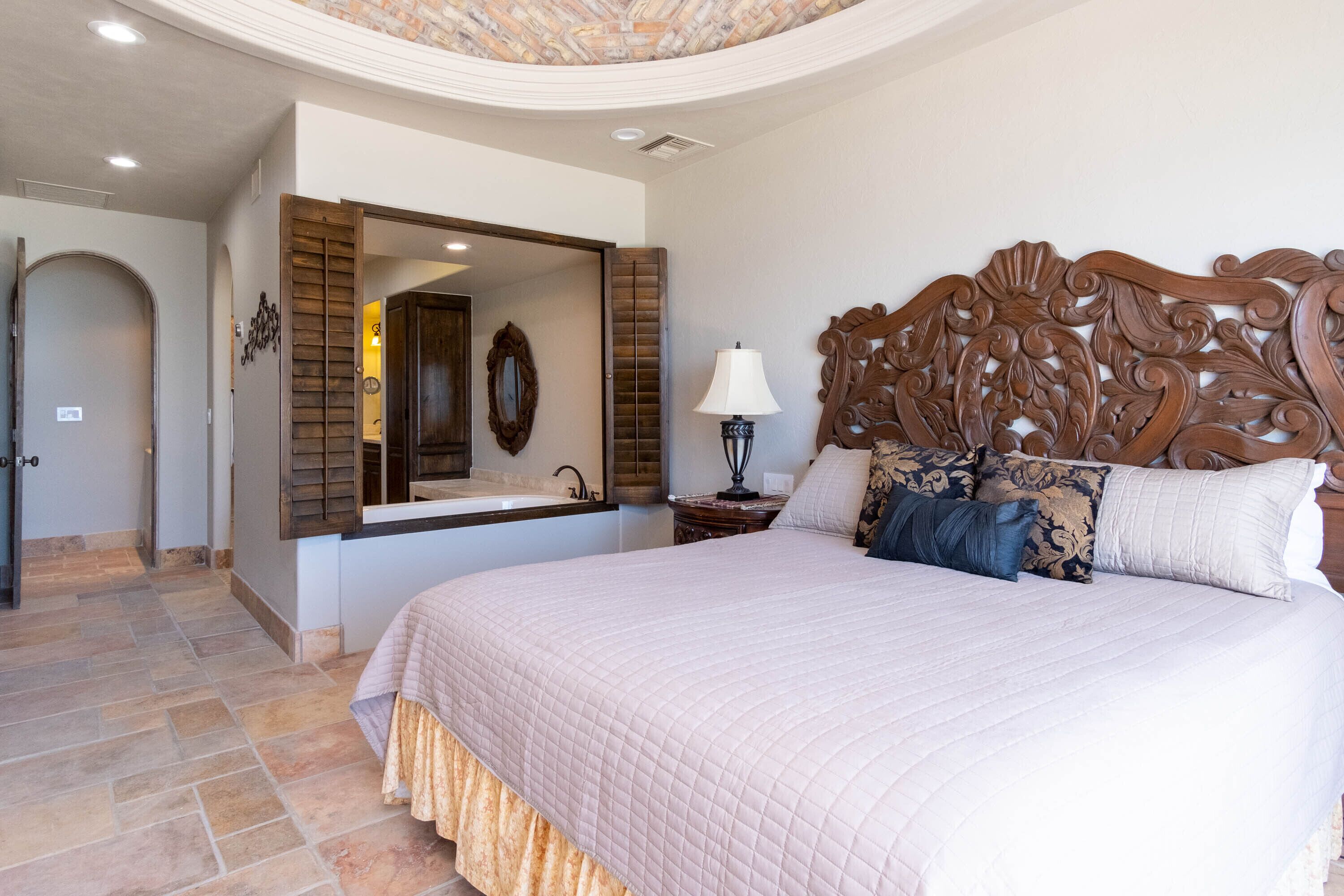 A bedroom with a large bed, a wooden headboard, a mirror, and a nightstand with a lamp.