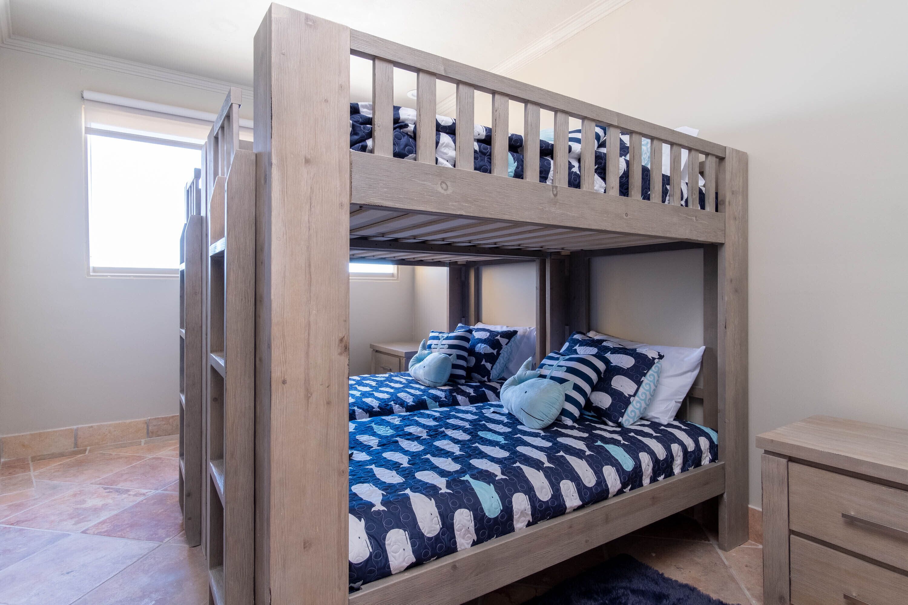 A bunk bed with a blue and white fish pattern bedspread, wooden headboard, and a small bedside table.