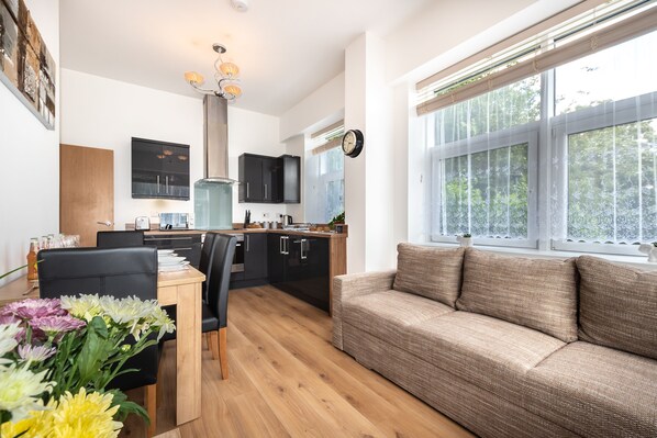 A modern kitchen with black cabinets, a wooden dining table, and a sofa by a large window.
