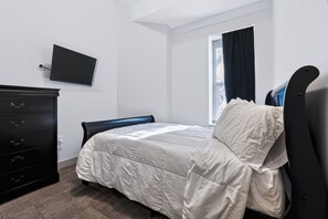 A bedroom with a bed, a dresser, a flat-screen TV, and a window with curtains. - Downtown Historic Warehouse District Lofts 301 (Cleveland)