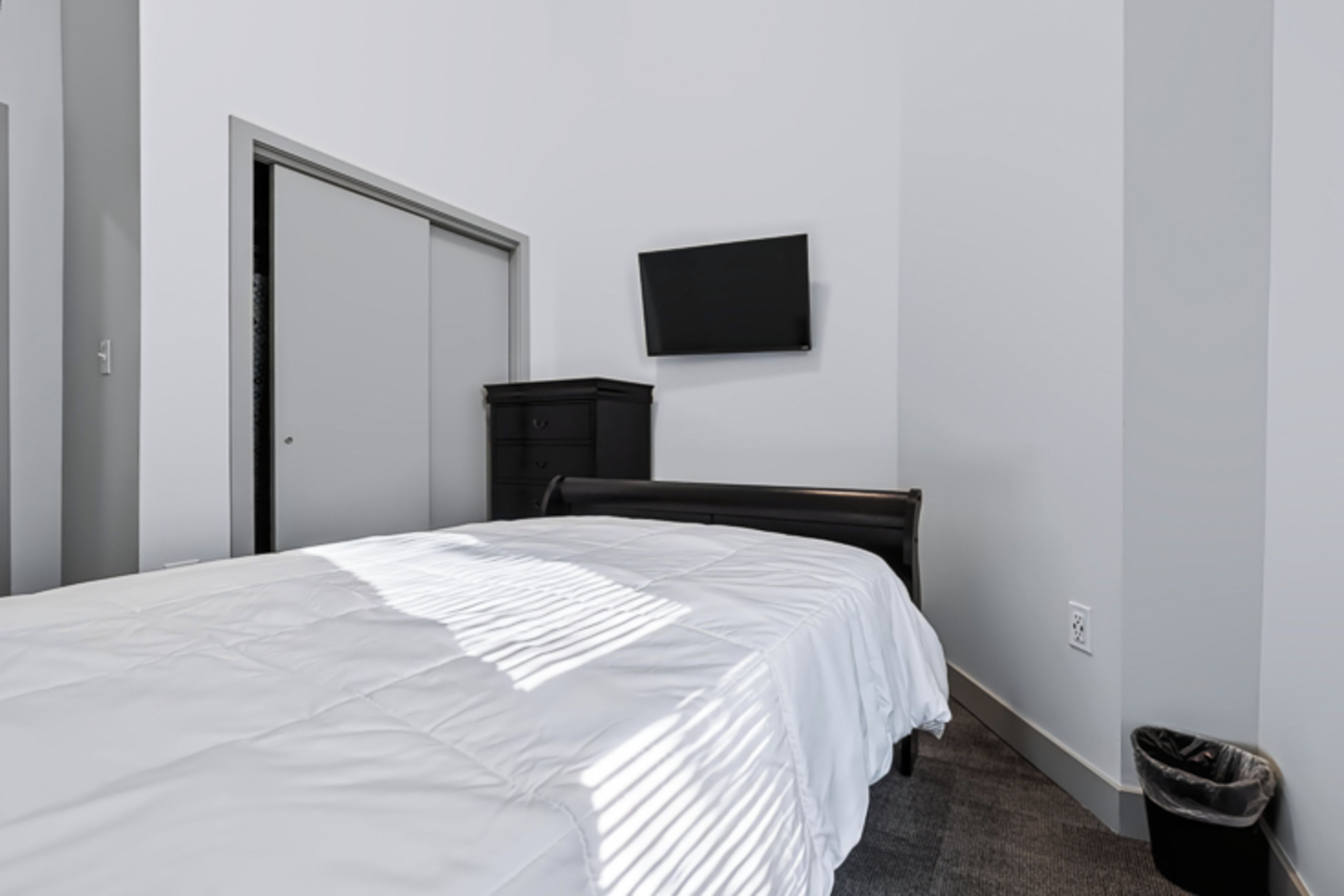 A bedroom with a bed, a dresser, a television on the wall, and a door.