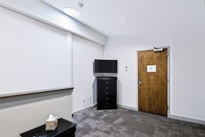 A room with a flat-screen TV on a black stand, a wooden door, and a small table with a tissue box. - Downtown Historic Warehouse District Lofts 301 (Cleveland)
