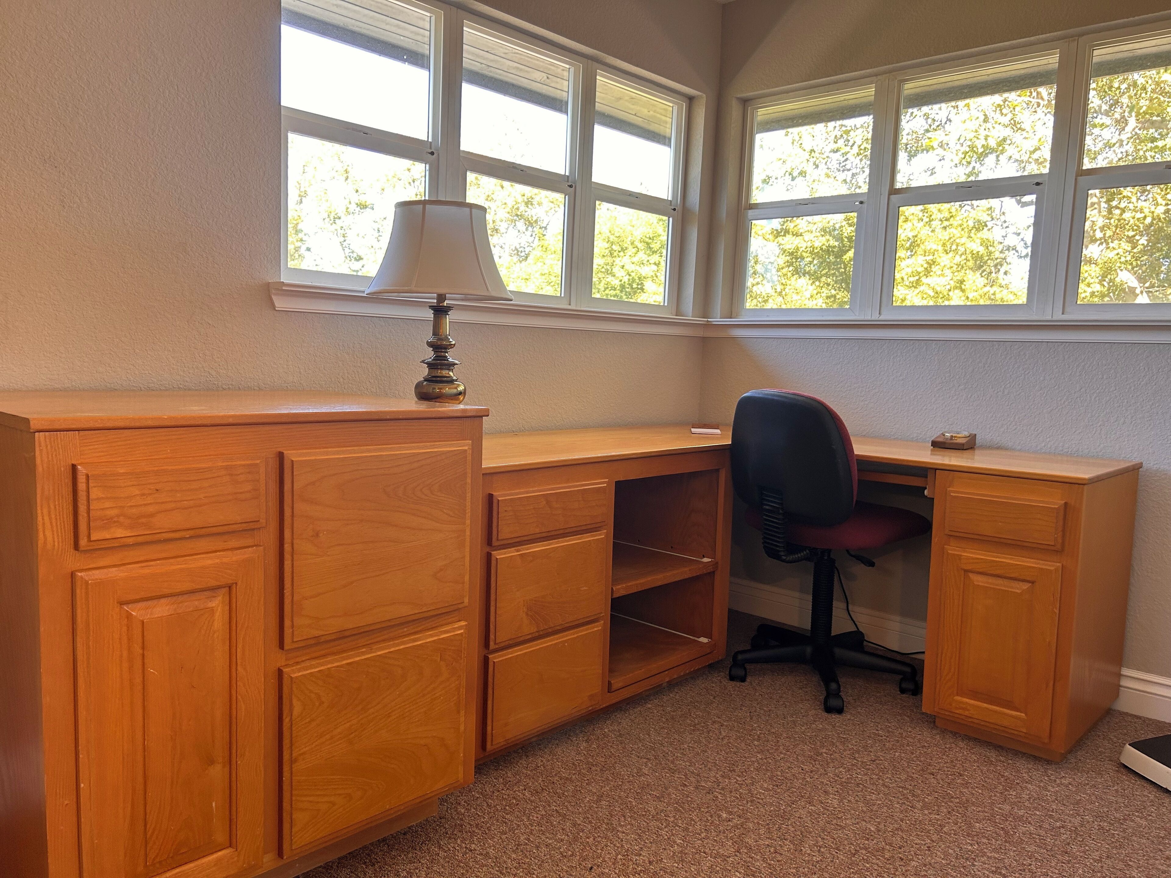 A wooden desk with a lamp, a chair, and a window with a view of trees.