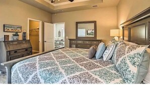A bedroom with a large bed, a ceiling fan, a dresser, a mirror, and a door leading to another room. - Ocean View  (Phoenix)