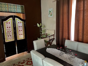 A dining area with a table set for two, a chair, a decorative table runner, and a plant.