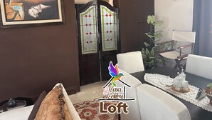 A living room with a sofa, a table with a lace tablecloth, a chair, a framed painting, and a decorative door with stained glass. - La Casa del Colibrí (Campeche)