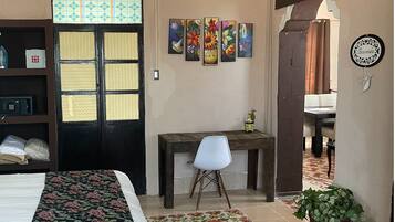Une chambre d’hôtel avec un lit, un bureau, une chaise et une porte agrémentée d’un paravent décoratif. On y trouve également des œuvres d’art murales et un panneau d’accueil.