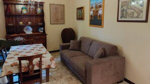 Una sala de estar con un sofá, una mesa de comedor con sillas, un candelabro y decoración en las paredes.
