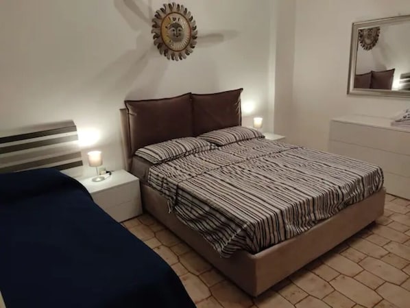 A bedroom with a bed, nightstands, a lamp, a mirror, and a decorative wall piece.