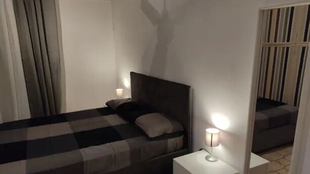 Un dormitorio con cama, mesitas de noche, un espejo y una ventana con cortinas.