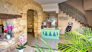 A lobby with a stone wall, a reception desk, a staircase, and potted plants.