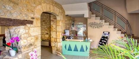 A lobby with a stone wall, a reception desk, a staircase, and potted plants.