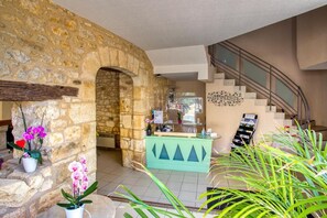 Un vestíbulo con pared de piedra, mostrador de recepción, escalera y plantas en macetas.