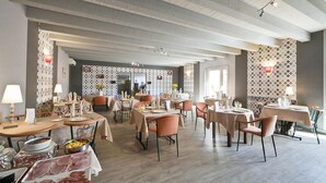 Un'ampia sala da pranzo con diversi tavoli e sedie, soffitto alto con travi a vista e pannelli decorativi alle pareti.