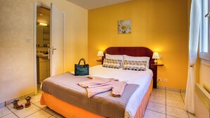 A hotel room with a bed, bedside lamps, a nightstand, a painting on the wall, and a door leading to a bathroom.