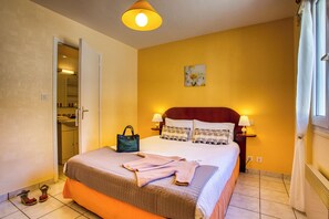 Habitación de hotel con cama, lámparas de noche, mesita de noche, un cuadro en la pared y una puerta que da a un baño.