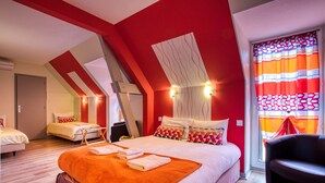 Una camera d'albergo con soffitto a falde, un letto grande con coperta arancione, una sedia e una finestra con tende a righe.