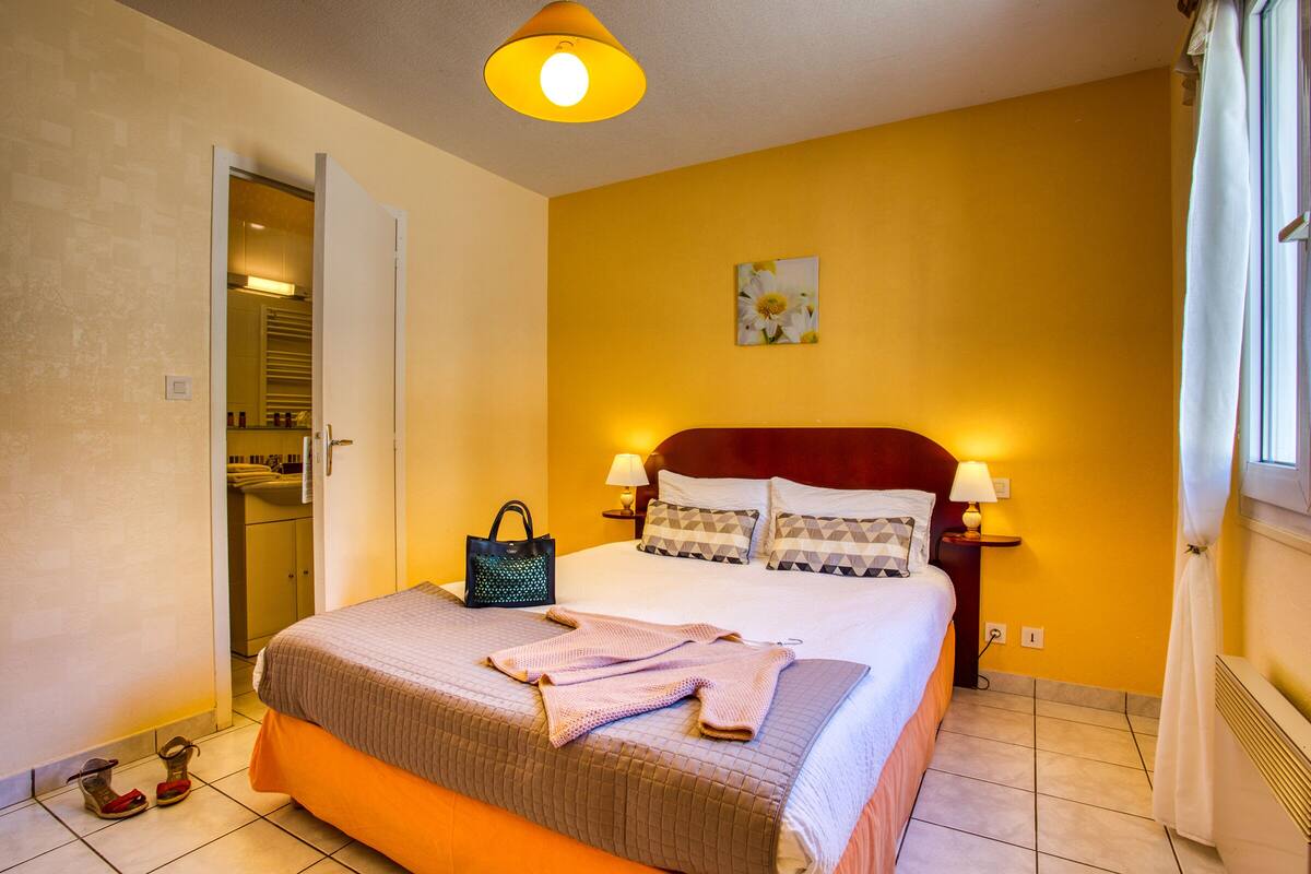 A hotel room with a bed, bedside lamps, a nightstand, a painting on the wall, and a door leading to a bathroom.