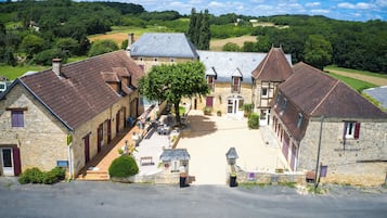 A traditional stone building with a courtyard, surrounded by lush greenery and a clear sky.