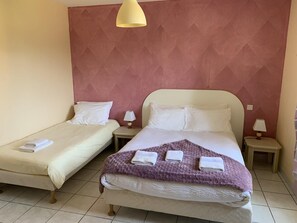 Habitación de hotel con dos camas individuales, cada una con una colcha blanca y una toalla doblada. Hay dos mesitas de noche con lámparas, y el papel tapiz de las paredes presenta un diseño geométrico.