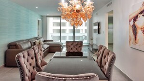 A modern living room with a glass coffee table, tufted chairs, and a chandelier. - Hollywood Beach Glam (Hollywood)