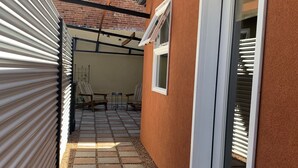 Kapea ulkokäytävä, jossa on tiiliseinä, liukuovi ja pieni patio, jossa on pöytä ja tuoleja.