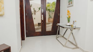 Ein Zimmer mit Holztür, einem kleinen Tisch mit Blumenvase und einem gerahmten Bild an der Wand.