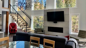 A modern living room with a staircase, a large TV, and a glass dining table. - Ski-Access and View Chair 5 Runs From Cabin in Brian Head, UT (Brian Head)