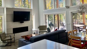 A spacious living room with a large TV mounted on the wall, a sofa, a coffee table, and a dining area with a glass table and wooden chairs. - Ski-Access and View Chair 5 Runs From Cabin in Brian Head, UT (Brian Head)