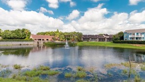 A serene lakeside view with a fountain, surrounded by residential buildings and lush greenery. - Spacious 4 Bedroom Condo Retreat! 🏠✨ (Kissimmee)