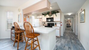 A modern kitchen with white cabinetry, a central island, and wooden chairs. - Spacious 4 Bedroom Condo Retreat! 🏠✨ (Kissimmee)