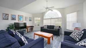A living room with a TV, sofa, coffee table, and a large window with blinds. - Spacious 4 Bedroom Condo Retreat! 🏠✨ (Kissimmee)