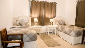 A bedroom with two beds, a wooden chair, a small table, and a nightstand with lamps.