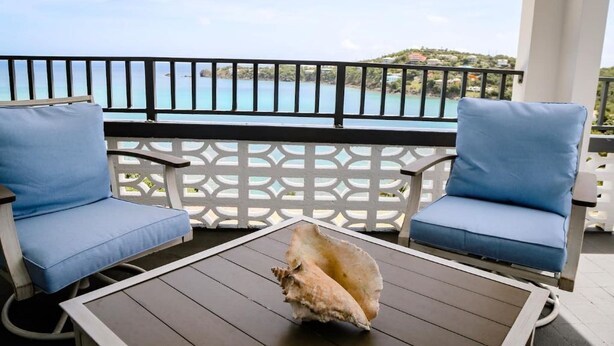 A balcony with two blue cushioned chairs, a wooden table, and a decorative shell.