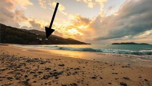A beach with a sunset, waves, and a mountain in the background.