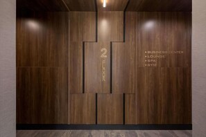Un intérieur moderne avec un mur décoré en bois, un grand chiffre « 2 » au centre, et un texte indiquant les équipements disponibles, tels qu’un centre d’affaires, un salon, un spa et une salle de sport.