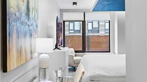Een moderne hotelkamer met een glazen bureau, een bed en een groot raam met uitzicht op de stad.