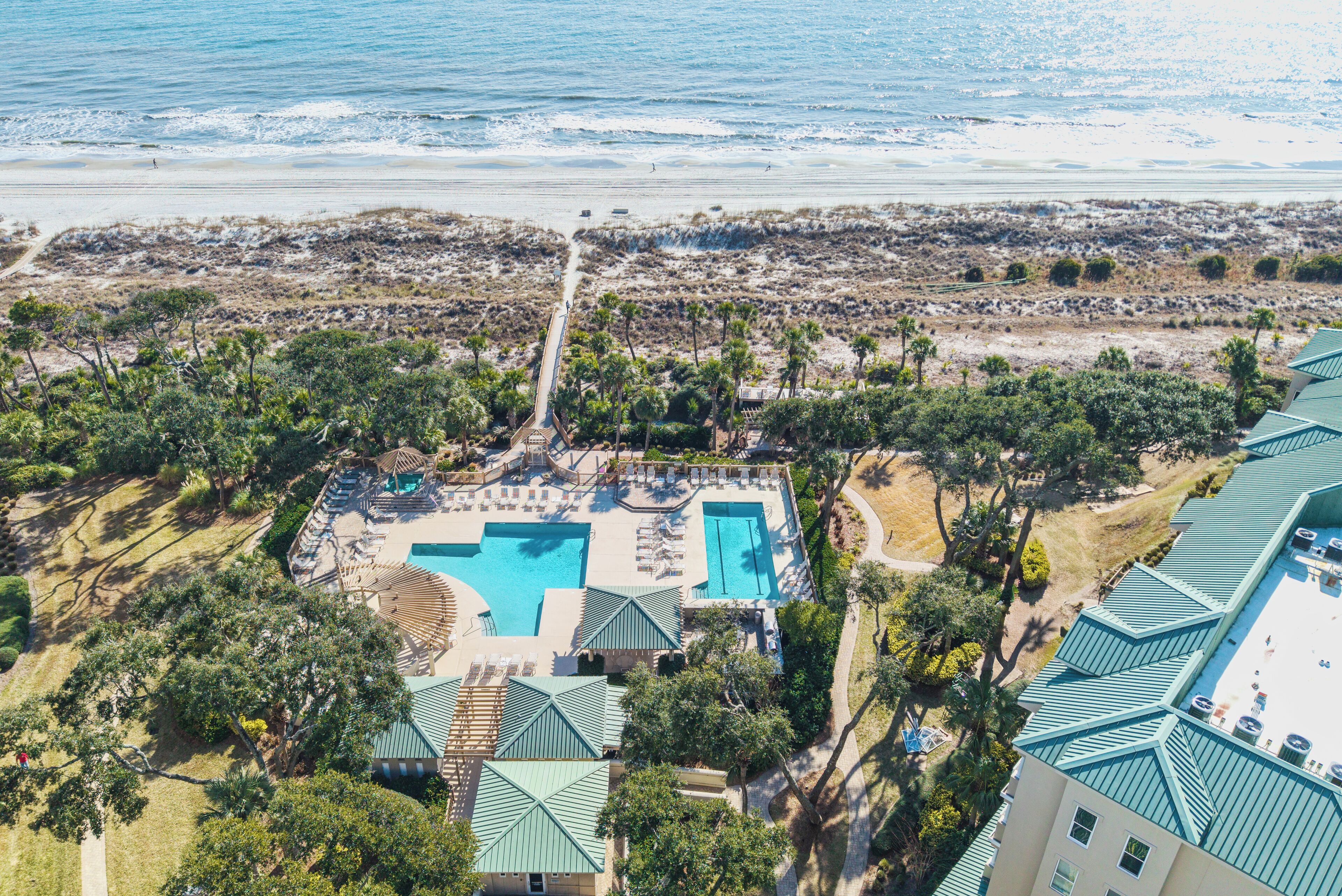 An aerial view of a resort with a large swimming pool, beach access, and lush greenery.