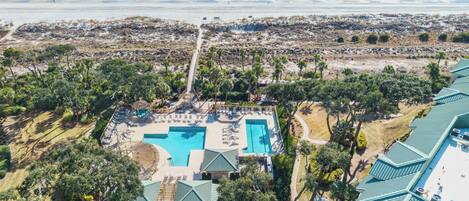 An aerial view of a resort with a large swimming pool, beach access, and lush greenery.