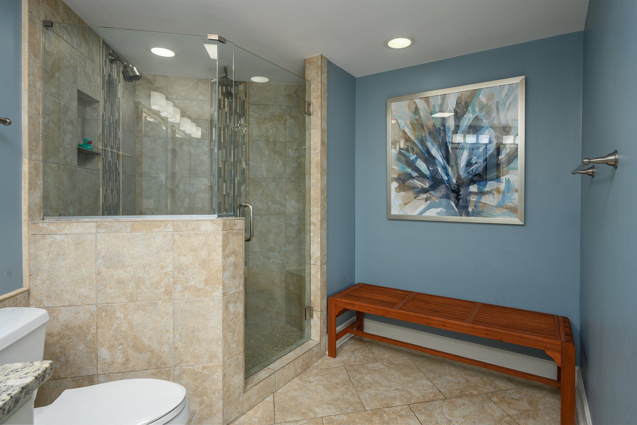 A bathroom with a glass-enclosed shower, a wooden bench, and a large abstract painting on the wall.