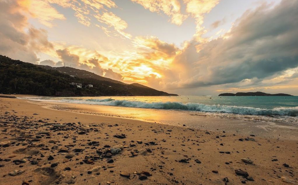 A beach with pebbles, waves, and a sunset.