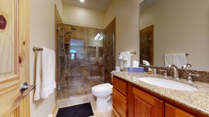 Ein Badezimmer mit einer gläsernen Duschkabine, einer weißen Toilette, einem Waschtisch mit Granitplatte und Holzschränken.