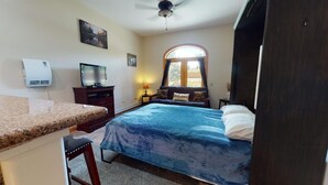 Ein Schlafzimmer mit Bett, Schreibtisch, Fernseher, Fenster und Deckenventilator.