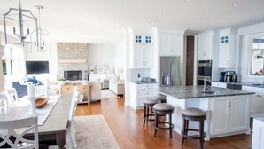 A modern kitchen with white cabinets, a central island with stools, a built-in oven, and a stone fireplace. - Glen Den Amazing Views of Sleeping Bear Dunes, Luxury Lakefront Home Glen Arbor (Empire)